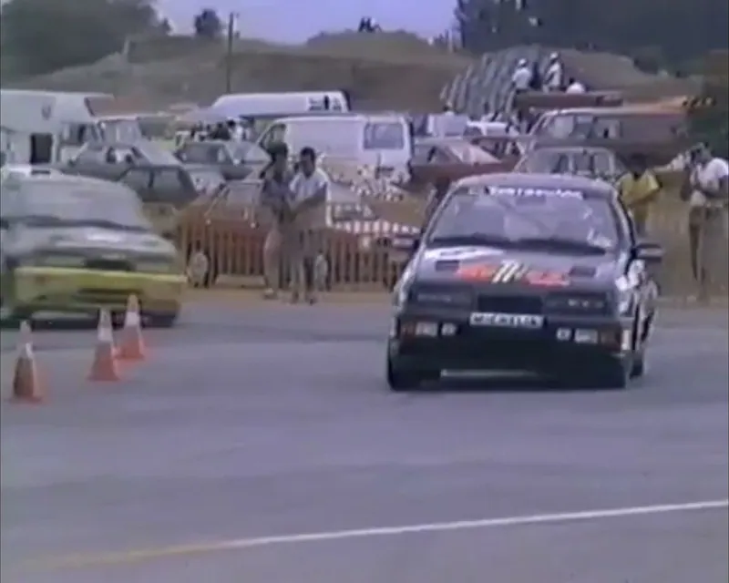 Καρέ από βίντεο αγώνα: σκούρο Ford Sierra δίπλα στους κώνους